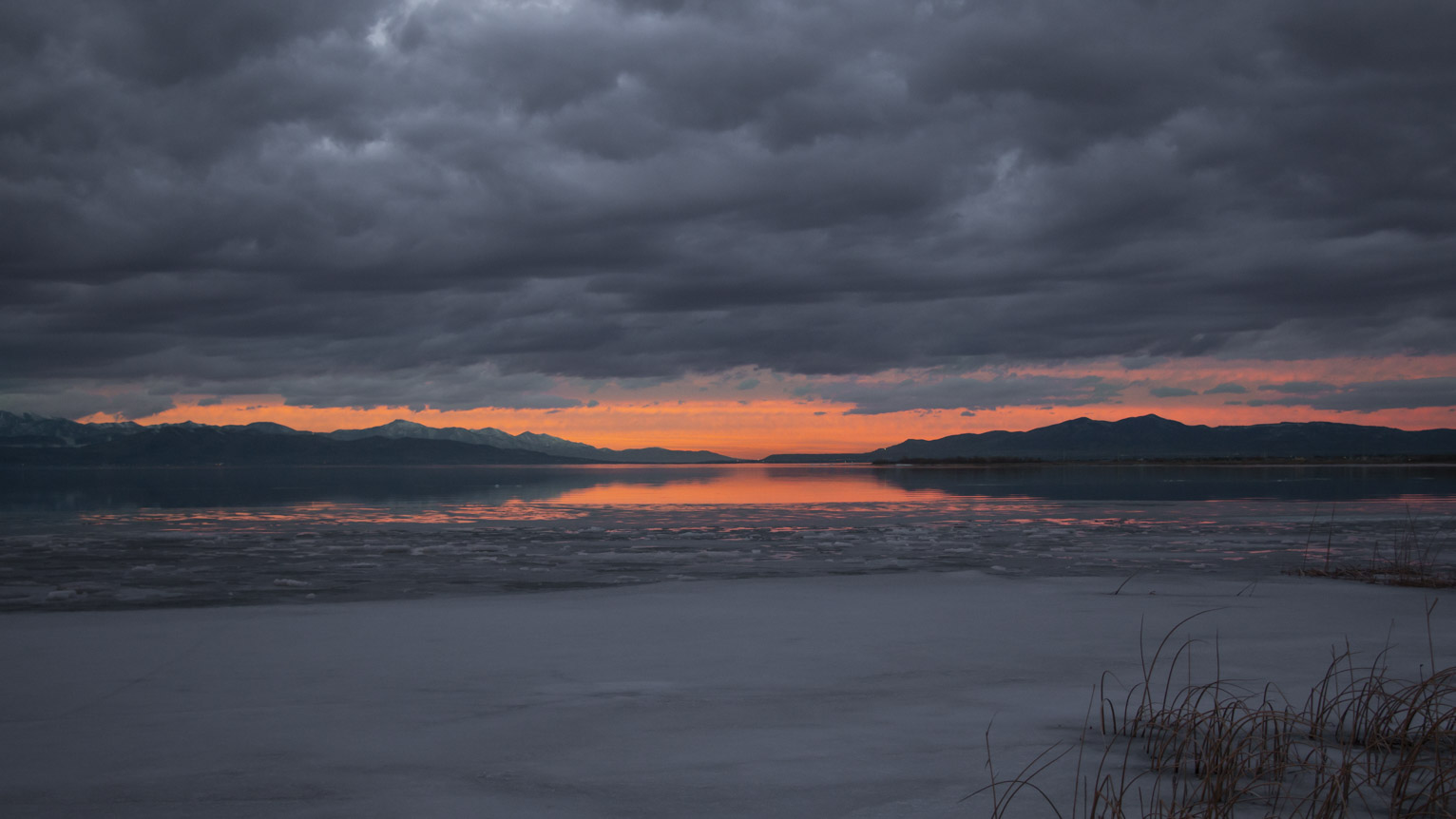 On the horizon the sky blazes orange and is reflected in the water until that gives way to ice, heavy grey purply textured clouds hang over